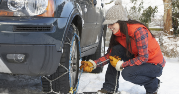 Femme installant des chaînes à neige sur sa voiture le long d'une route enneigée